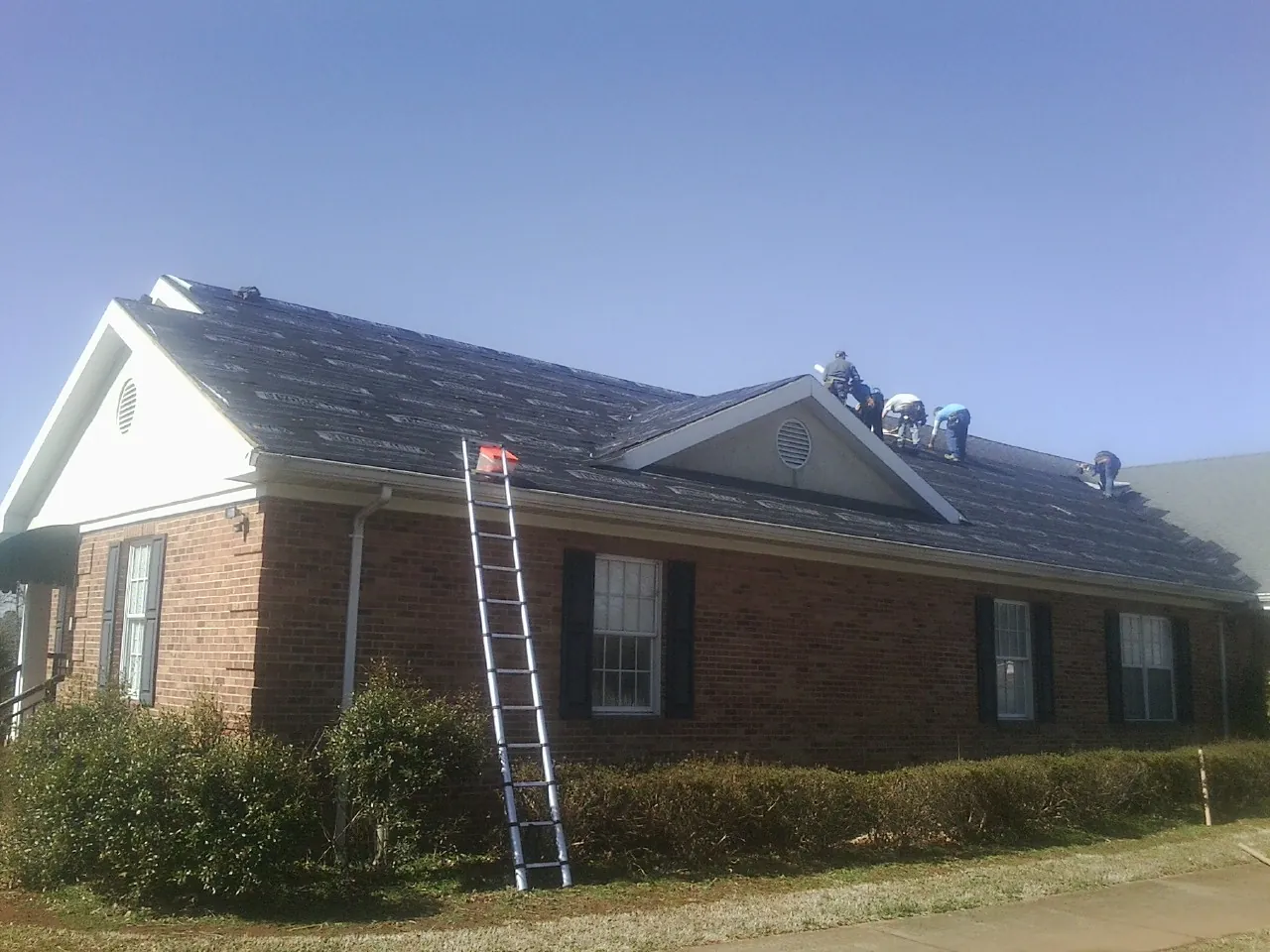 Crew tearing shingles off a brick ranch roof with a ladder set — Metal Roof Repair work by our crew in Richfield